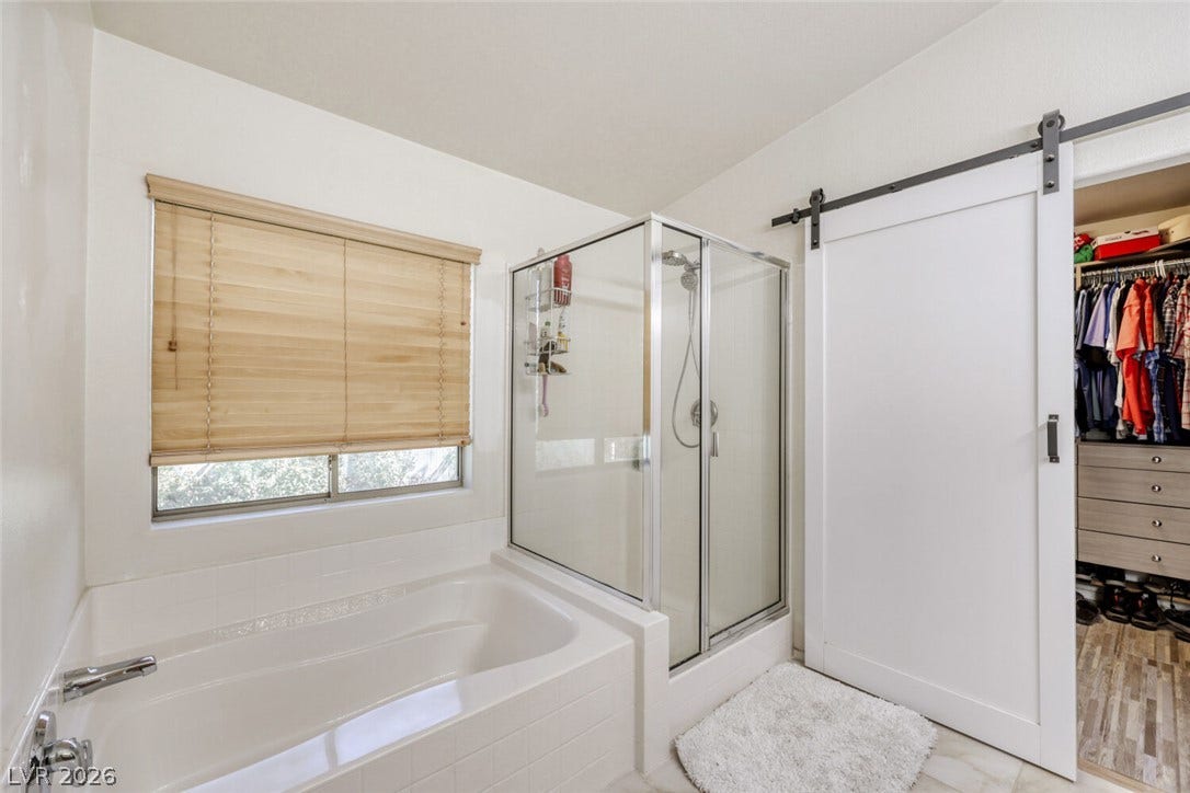 5817 Hawkeye Bell Street, North Las Vegas, NV 89081 A glass-enclosed shower stands alongside a deep soaking tub beneath a large window.