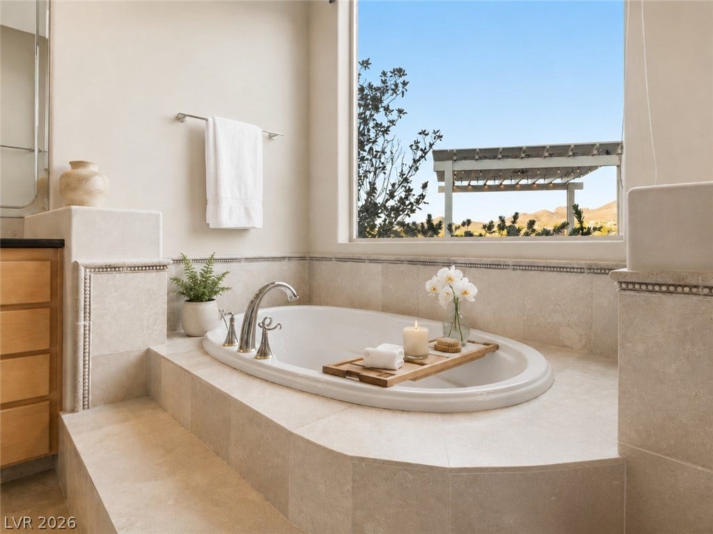 6 Brookridge Drive, Henderson, NV 89052 A deep soaking tub sits framed by elegant stone tile and a scenic picture window.