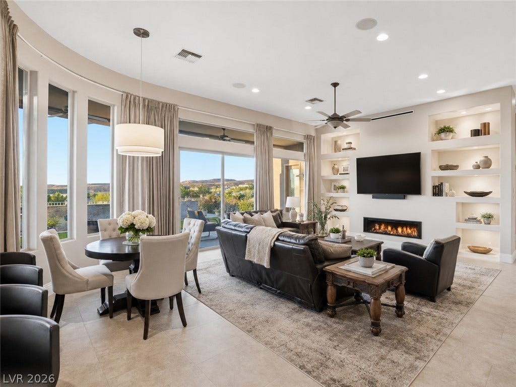 6 Brookridge Drive, Henderson, NV 89052 A spacious open-concept interior features tall curved windows and built-in shelving beside a modern fireplace.