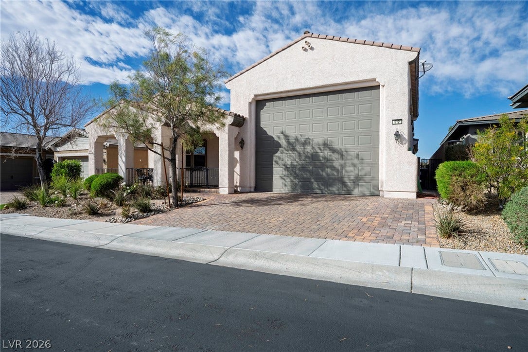 A spacious garage fronted by a classic paver driveway highlights this stucco home design.