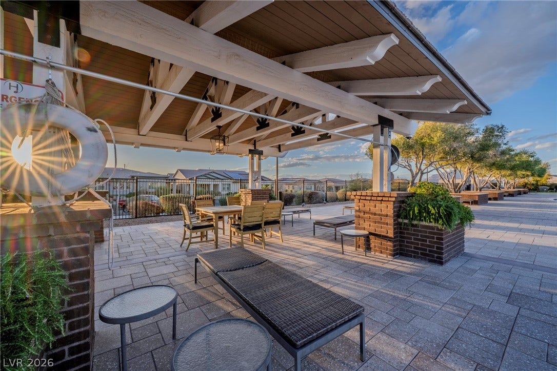 An inviting covered patio features warm wood ceiling beams and expansive stone paver flooring.