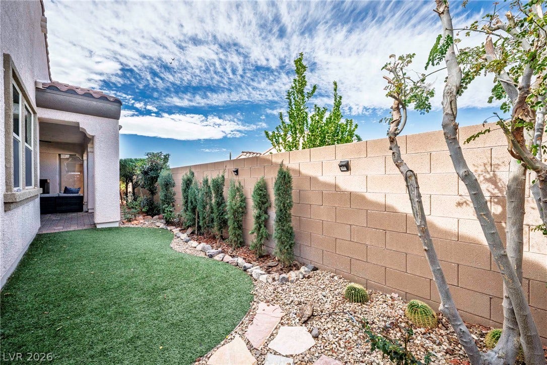A block wall borders the private backyard containing a neat lawn and stone-bordered landscaping.
