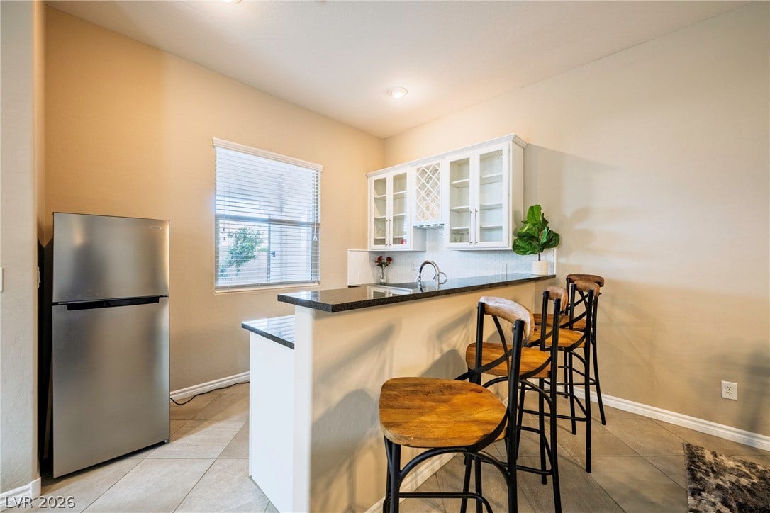 A wet bar features granite counters and built-in glass cabinetry over durable tile flooring.