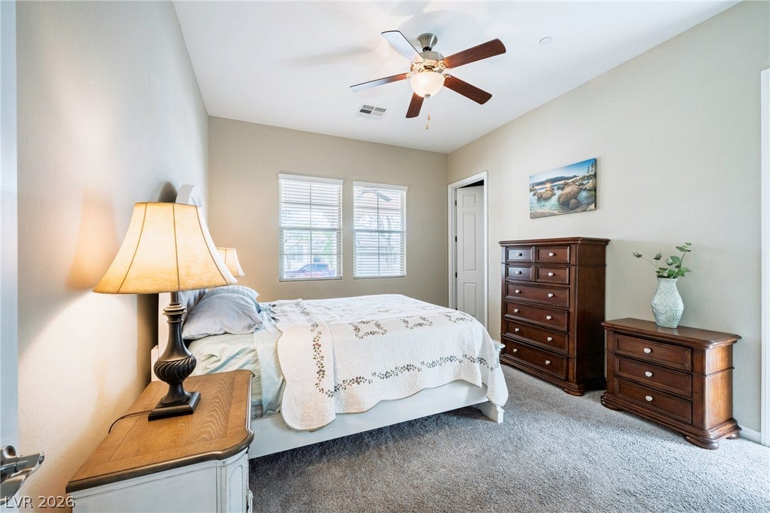 A quiet bedroom retreat highlights neutral walls, textured carpeting, and double windows.