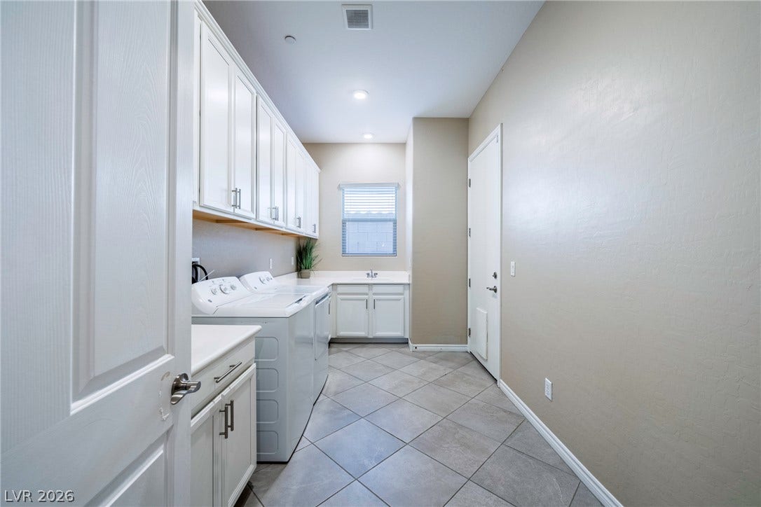 Ample white cabinetry and durable tile flooring highlight this functional laundry utility area.
