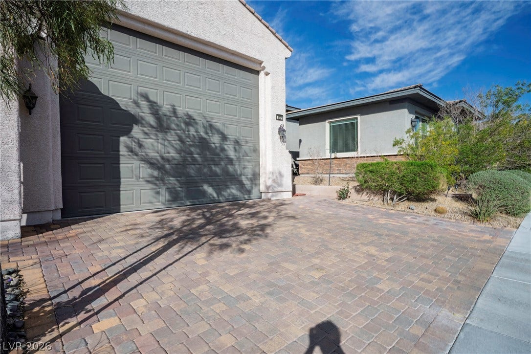 A spacious paver driveway leads to the attached garage under clear blue skies.