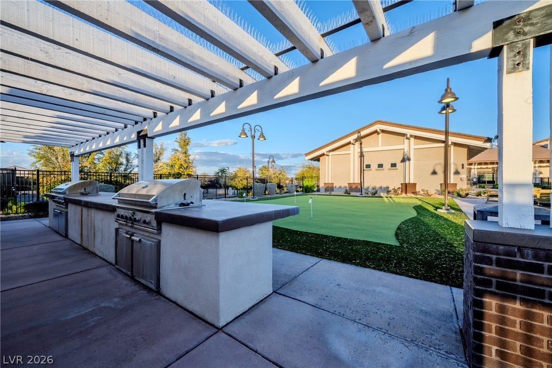An outdoor kitchen with built-in grills sits beneath a pergola near a putting green.
