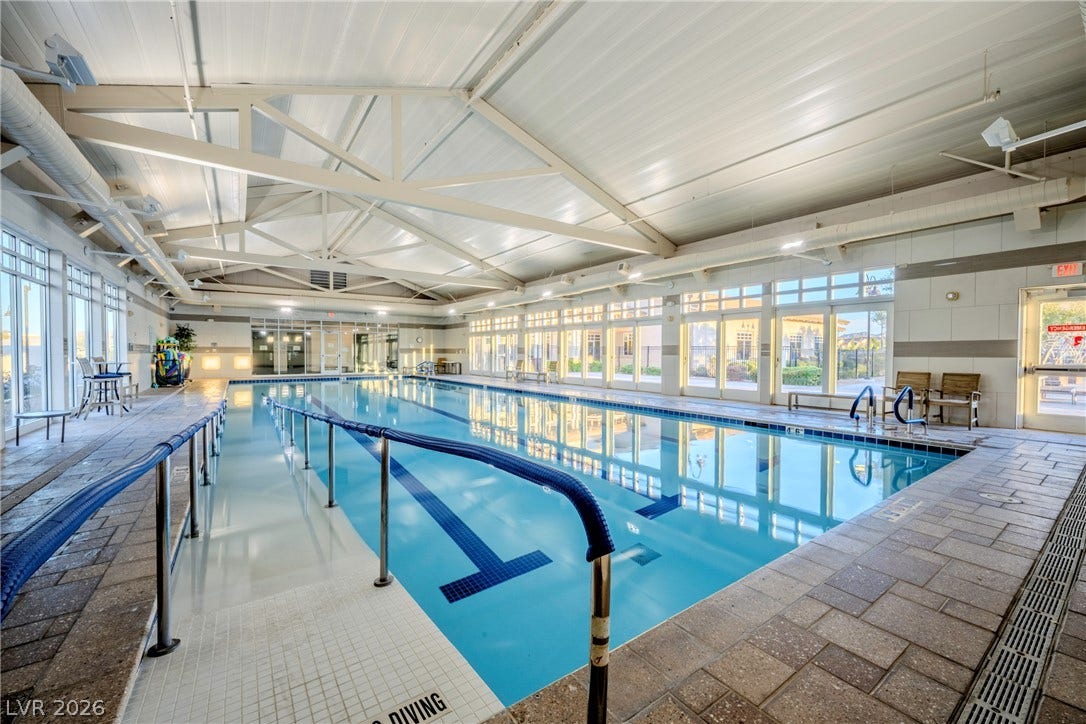An expansive indoor swimming pool sits beneath high vaulted ceilings and a structural truss system.