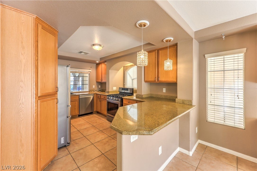 10744 Teton Village Court, Henderson, NV 89052 Warm wooden cabinetry and polished stone countertops elevate this functional kitchen layout.