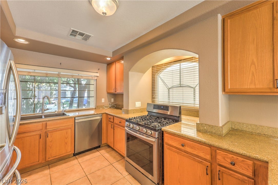 10744 Teton Village Court, Henderson, NV 89052 Warm wood cabinetry and stone countertops wrap around this efficient, well-lit kitchen space.