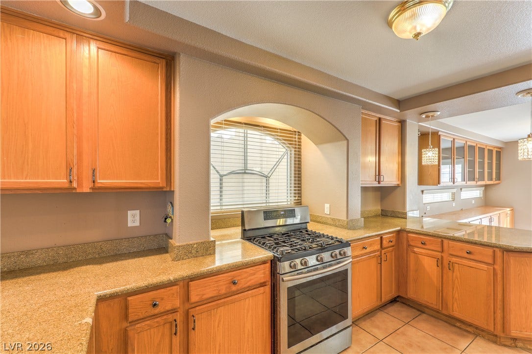 10744 Teton Village Court, Henderson, NV 89052 Warm wood cabinetry and granite countertops frame a built-in gas range nestled under an arched alcove.