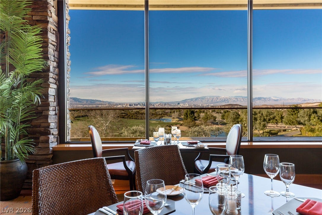 18 Wade Hampton Trail, Henderson, NV 89052 Floor-to-ceiling windows frame sweeping mountain and city views beyond the stone-accented dining space.