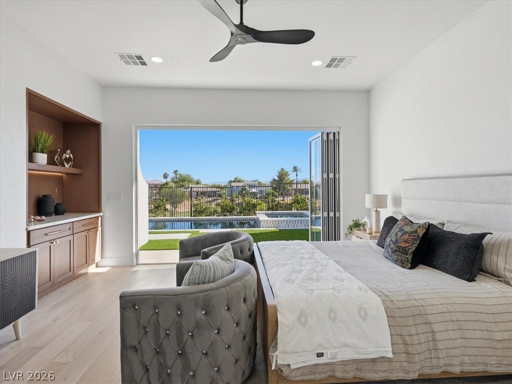 3074 Soft Horizon Way, Las Vegas, NV 89135 An inviting bedroom with wide-plank wood flooring and a refreshing pool vista from large folding doors.