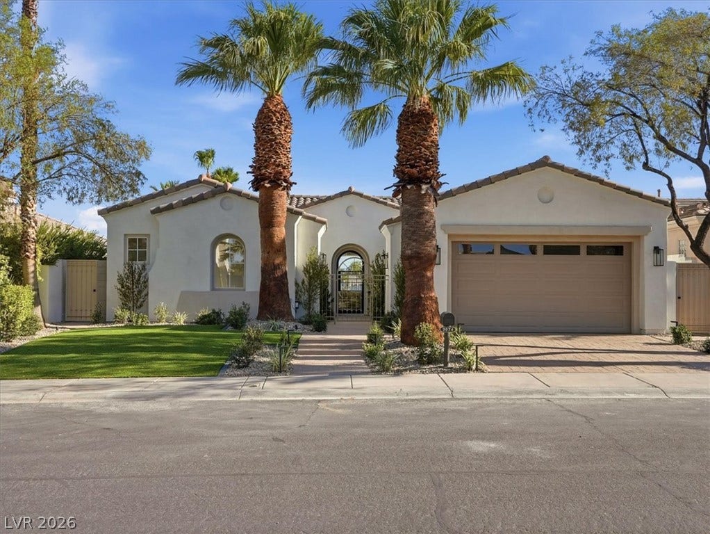 3074 Soft Horizon Way, Las Vegas, NV 89135 A charming stucco home welcomes with lush green lawn, mature palm trees, and a spacious paver driveway leading to an attached garage.
