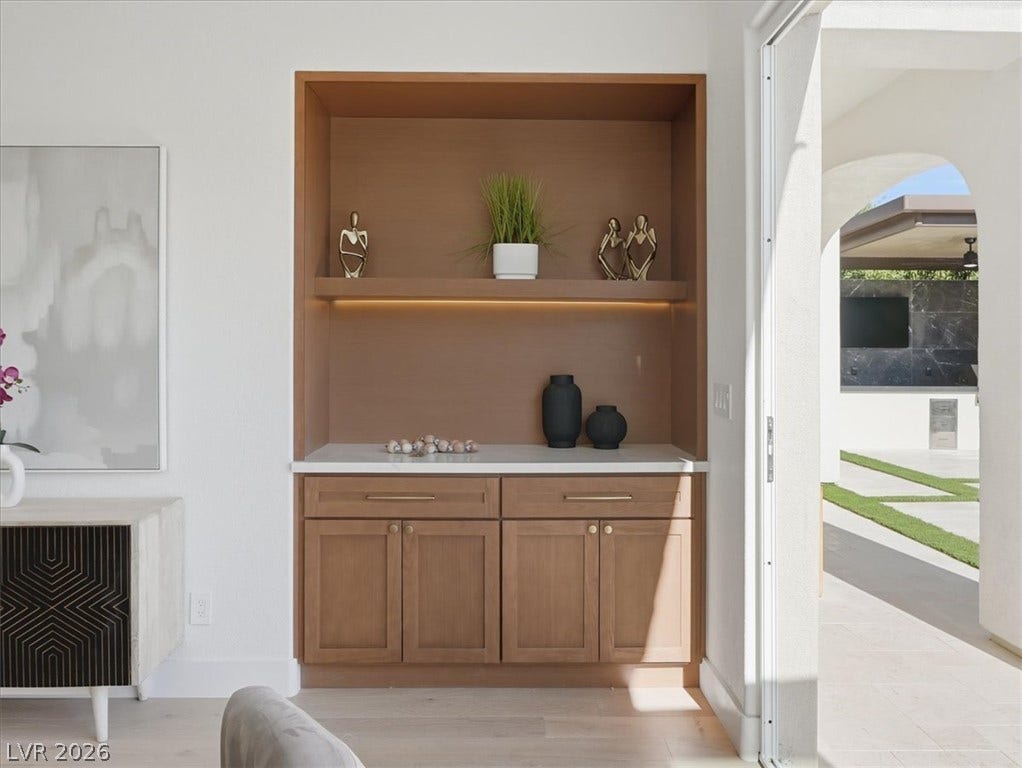 3074 Soft Horizon Way, Las Vegas, NV 89135 Built-in shelving and cabinetry offer convenient storage, leading to an open-air outdoor living space with manicured grass and a dark-tiled outdoor feature.