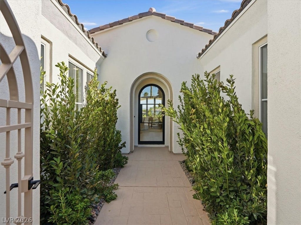 3074 Soft Horizon Way, Las Vegas, NV 89135 An inviting arched entryway leads to a chic, glass-paned front door, framed by verdant shrubs and classic Mediterranean architecture.