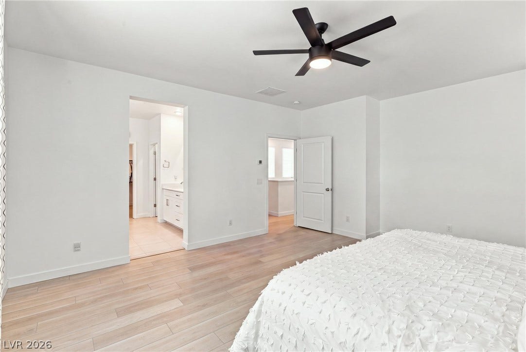 709 Emerson Creek Court, North Las Vegas, NV 89084 A well-lit bedroom features a ceiling fan, light wood flooring, and an adjoining bath with a double vanity.