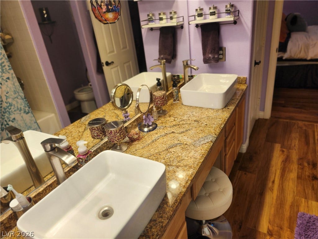 A spacious vanity features dual vessel sinks set on polished granite countertops alongside wood-look flooring.
