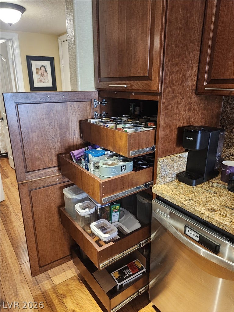 Rich wood cabinetry features pull-out pantry shelving next to a granite-topped prep space.