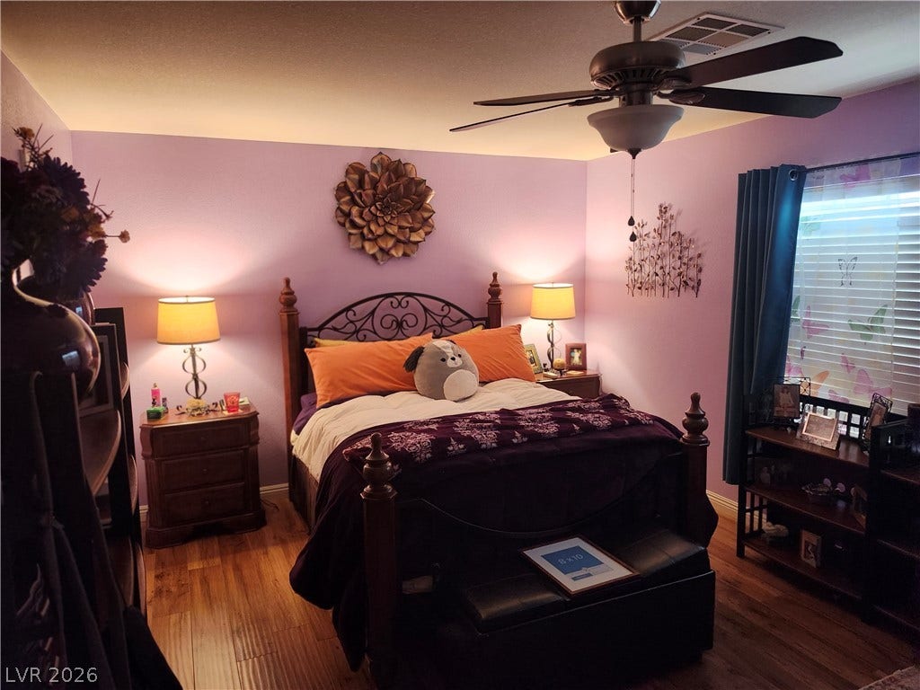 Gleaming hardwood floors and a wide window with plantation shutters define this inviting bedroom space.