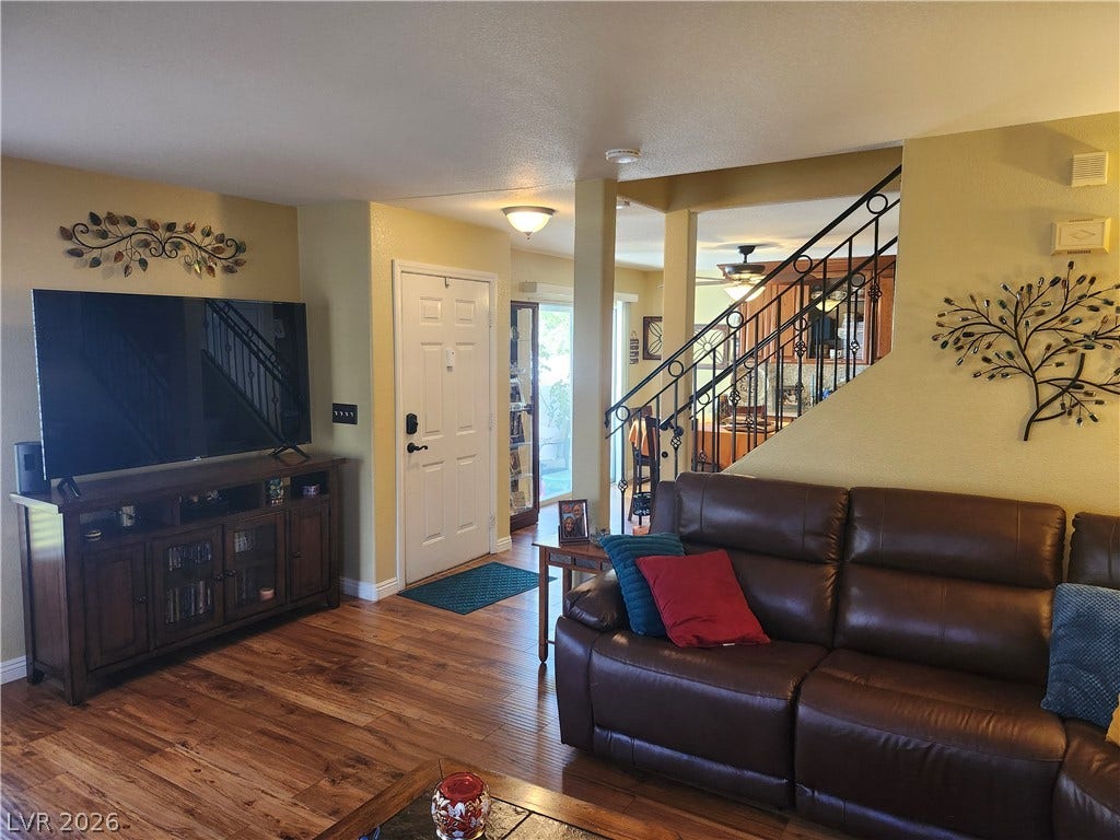 Rich wood-look flooring and an ornate wrought-iron staircase anchor this welcoming living area.