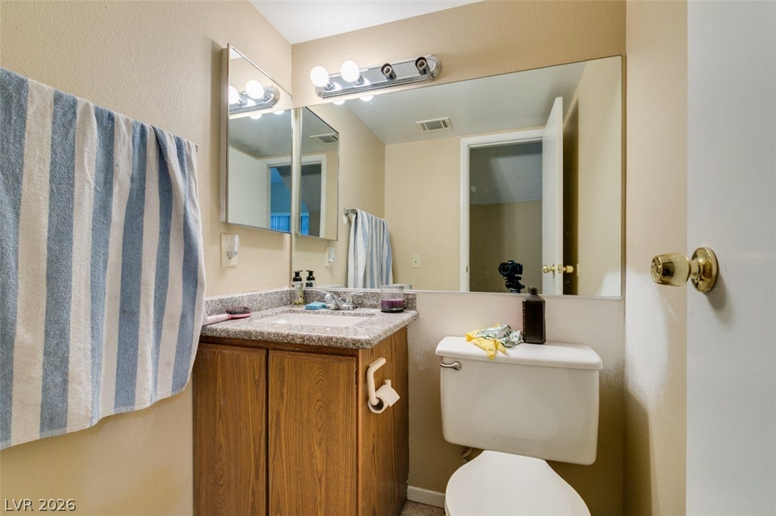 A classic wooden vanity matches with a stone countertop beneath a large mirror.