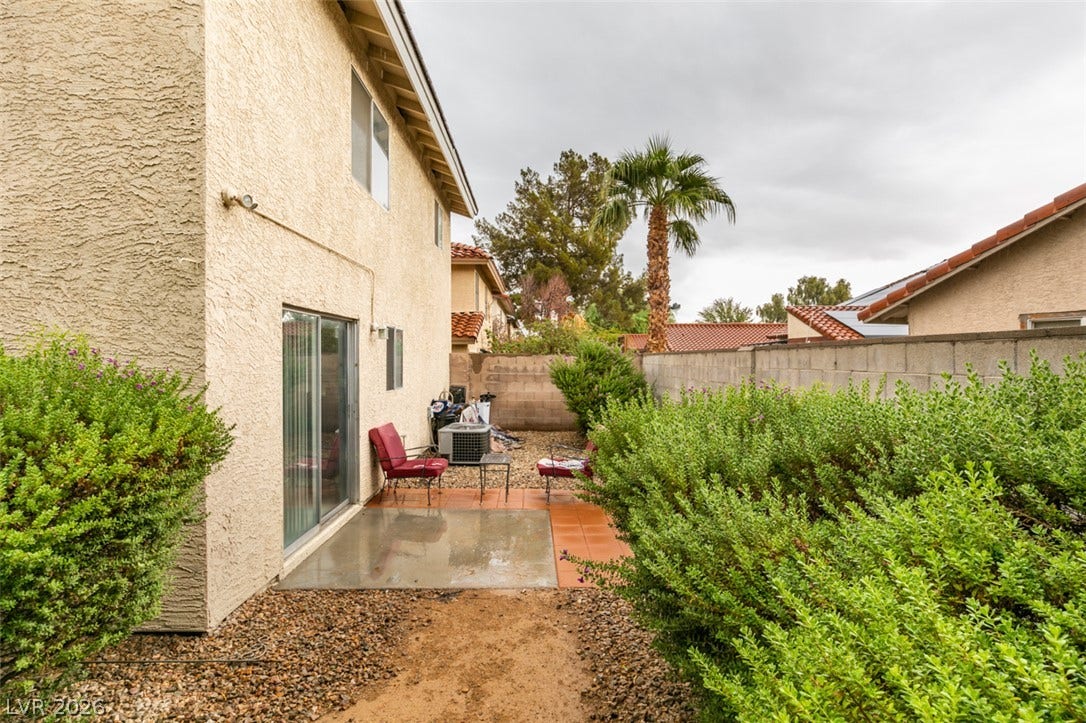 Lush perimeter plantings frame the concrete patio area of this stucco exterior.