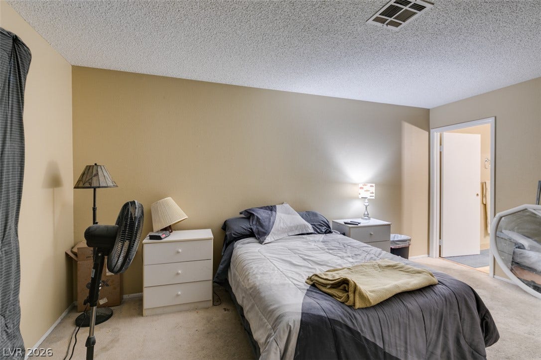 An open doorway leads from this carpeted bedroom toward an adjacent bath area.