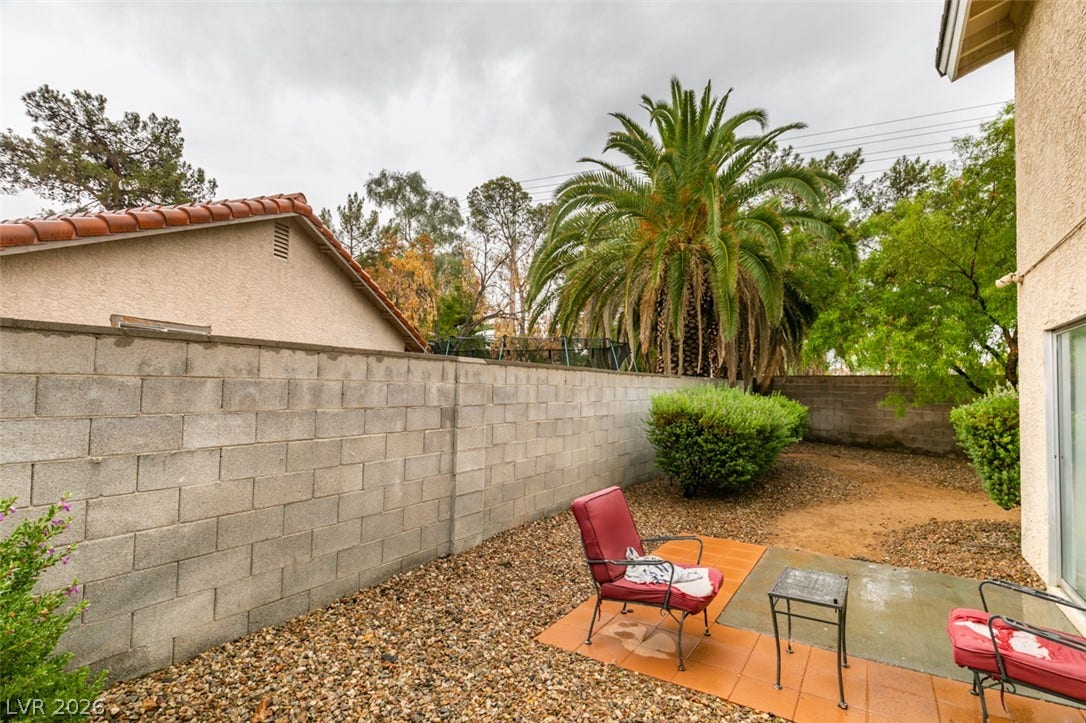 A private block-walled backyard features tiled patio areas alongside low-maintenance gravel landscaping.