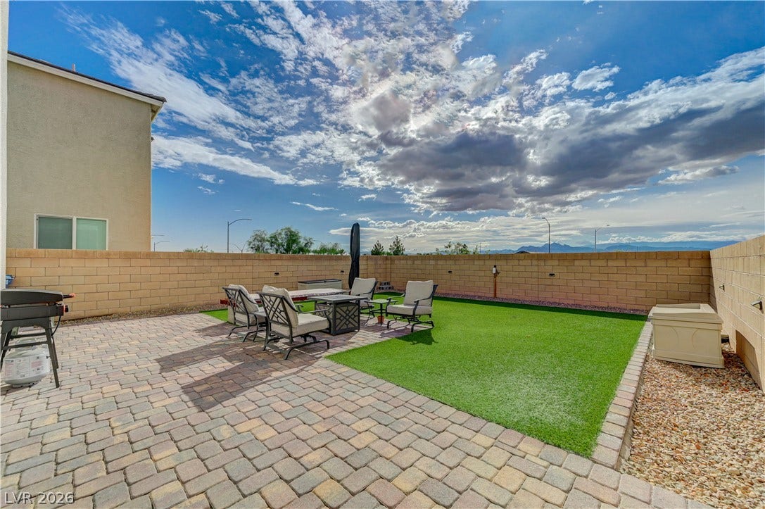 6629 Rockhouse Street, North Las Vegas, NV 89086 Block fencing encloses a low-maintenance backyard featuring a paver patio and green turf area.