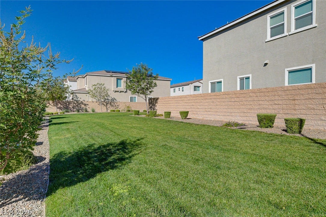 6629 Rockhouse Street, North Las Vegas, NV 89086 A spacious green lawn is bordered by a clean masonry privacy wall under clear blue skies.