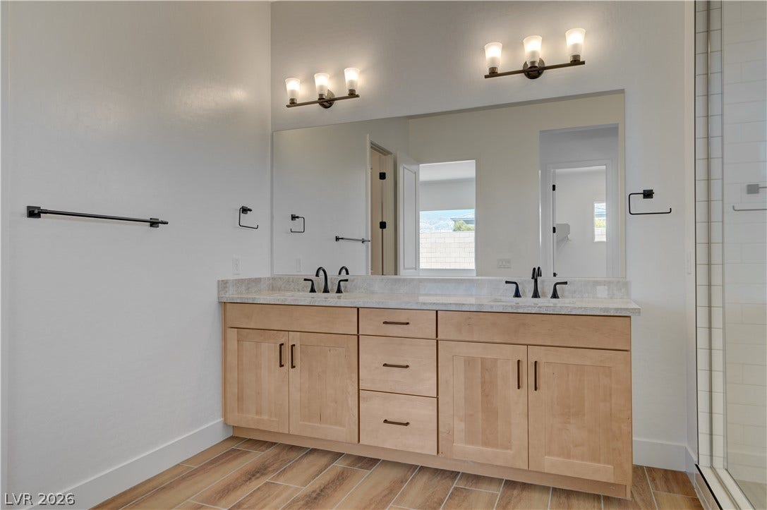 5689 Searching Bear Court, Las Vegas, NV 89149 A well-appointed bathroom features a double vanity with granite counters and rich wood cabinetry, alongside a spacious mirror.