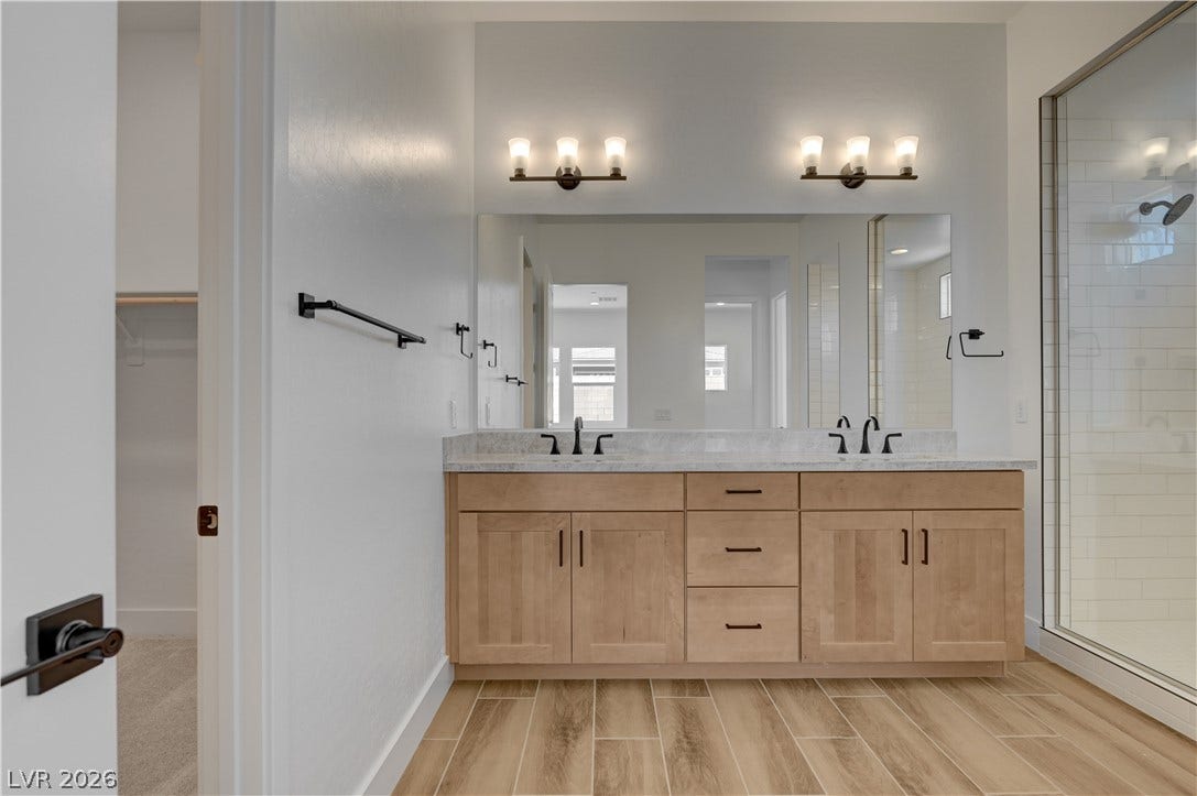 5689 Searching Bear Court, Las Vegas, NV 89149 A well-appointed primary bathroom showcases a double vanity, elegant countertops, and a spacious glass-enclosed shower.