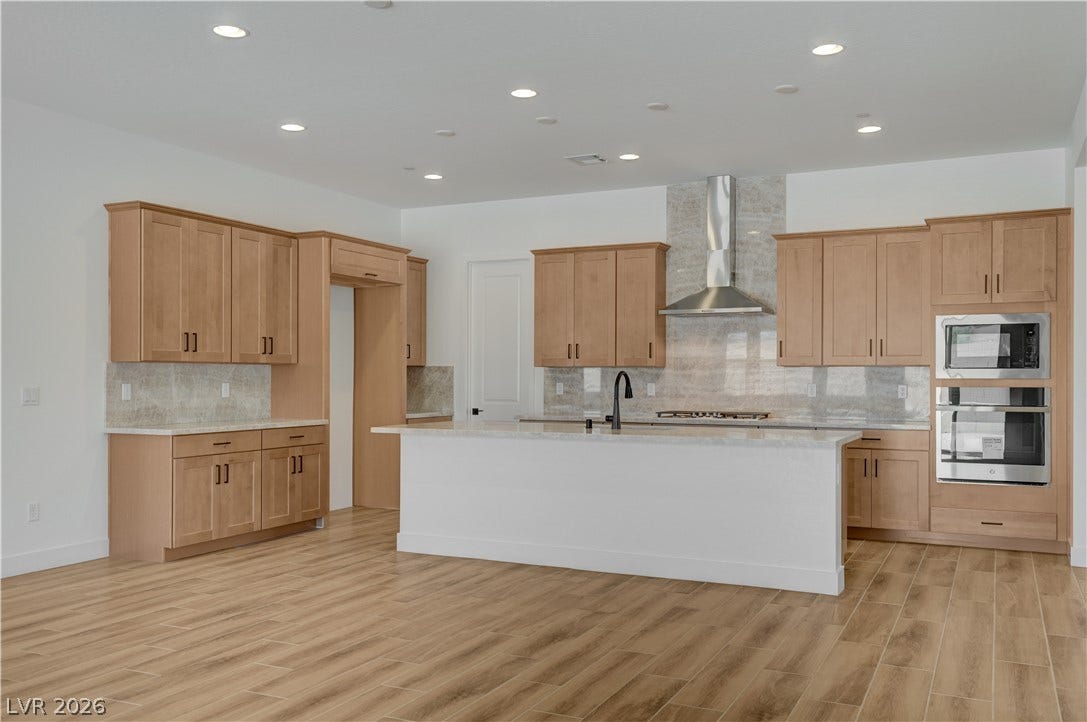 5689 Searching Bear Court, Las Vegas, NV 89149 A well-appointed kitchen features a central island, light wood cabinetry, stainless steel appliances, and wood-look tile flooring.