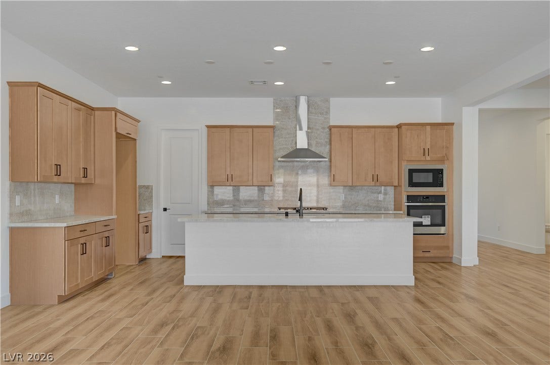 5689 Searching Bear Court, Las Vegas, NV 89149 A contemporary kitchen features light wood cabinetry, recessed lighting, and an elegant stone-look backsplash.