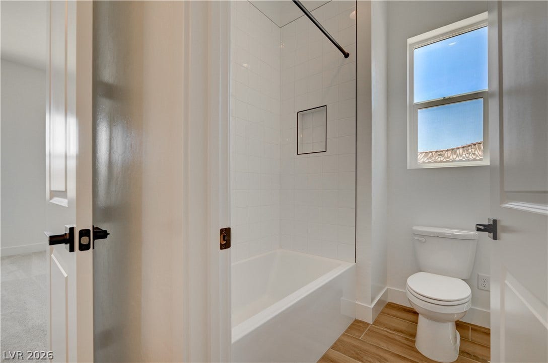 5689 Searching Bear Court, Las Vegas, NV 89149 A well-lit bathroom features a pristine white bathtub, subway tile shower, and wood-look tile flooring.