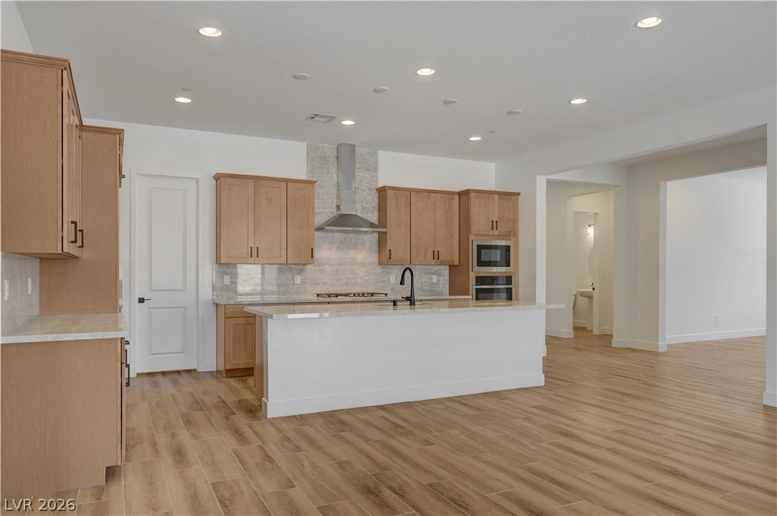 5689 Searching Bear Court, Las Vegas, NV 89149 An open concept kitchen features warm-toned cabinetry, light stone countertops, and wood-look tile flooring.