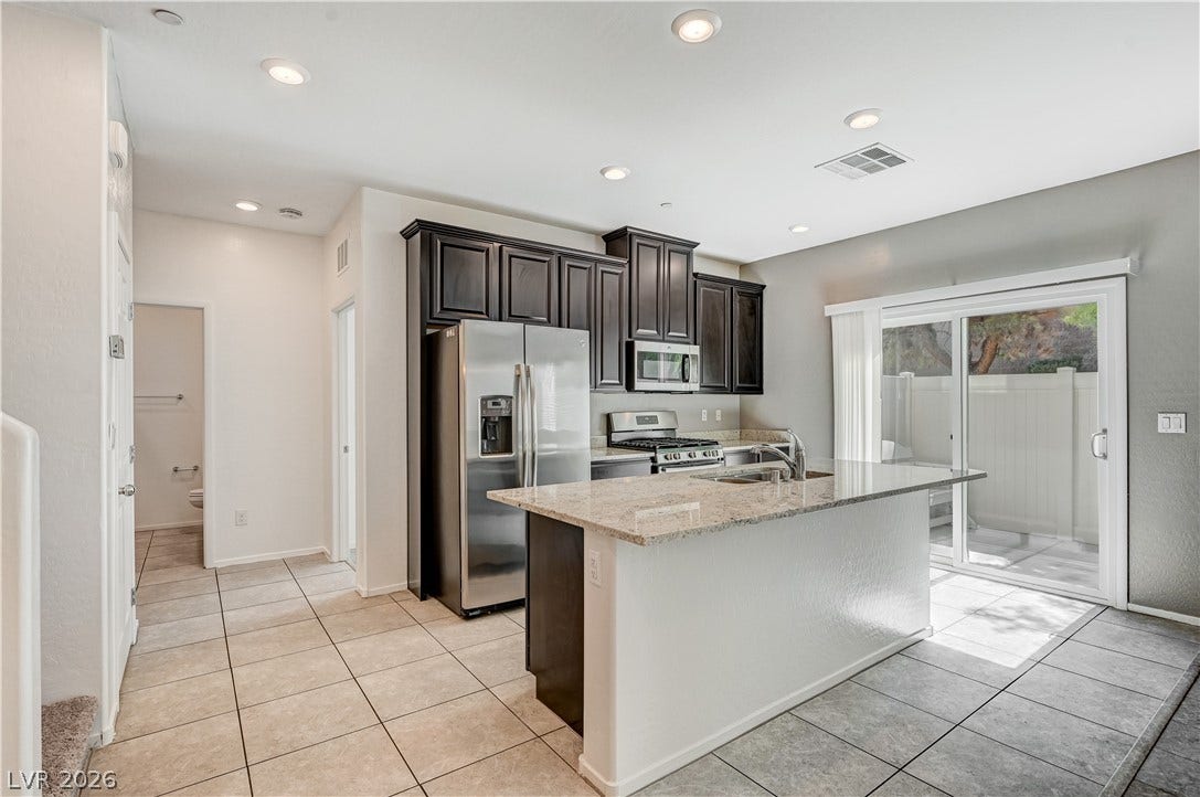 2455 Sunflower Days Avenue, #1056, North Las Vegas, NV 89031 Granite countertops and dark cabinetry anchor this kitchen space with access to the patio.