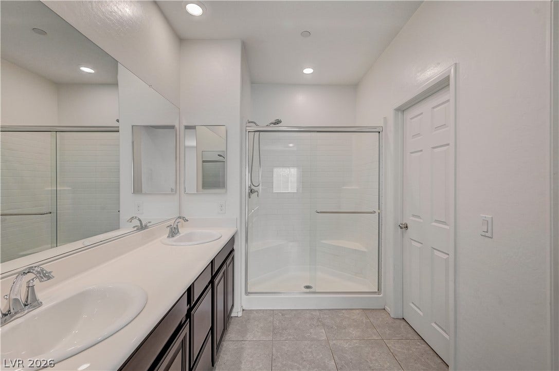 2455 Sunflower Days Avenue, #1056, North Las Vegas, NV 89031 Recessed lighting illuminates a spacious bathroom featuring a dual vanity and glass-enclosed shower.
