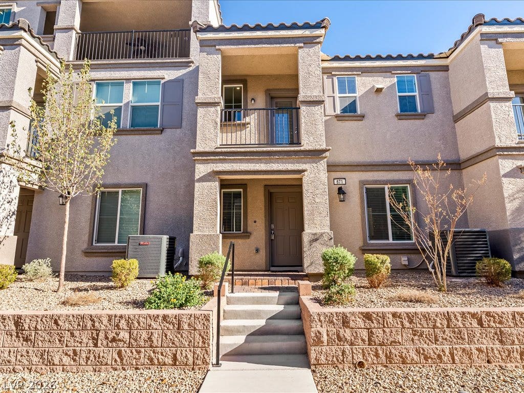 671 Foam Flower Lane, Henderson, NV 89015 Multi-level stucco exterior showcases private balconies and tiered stone retaining walls flanking the entrance.