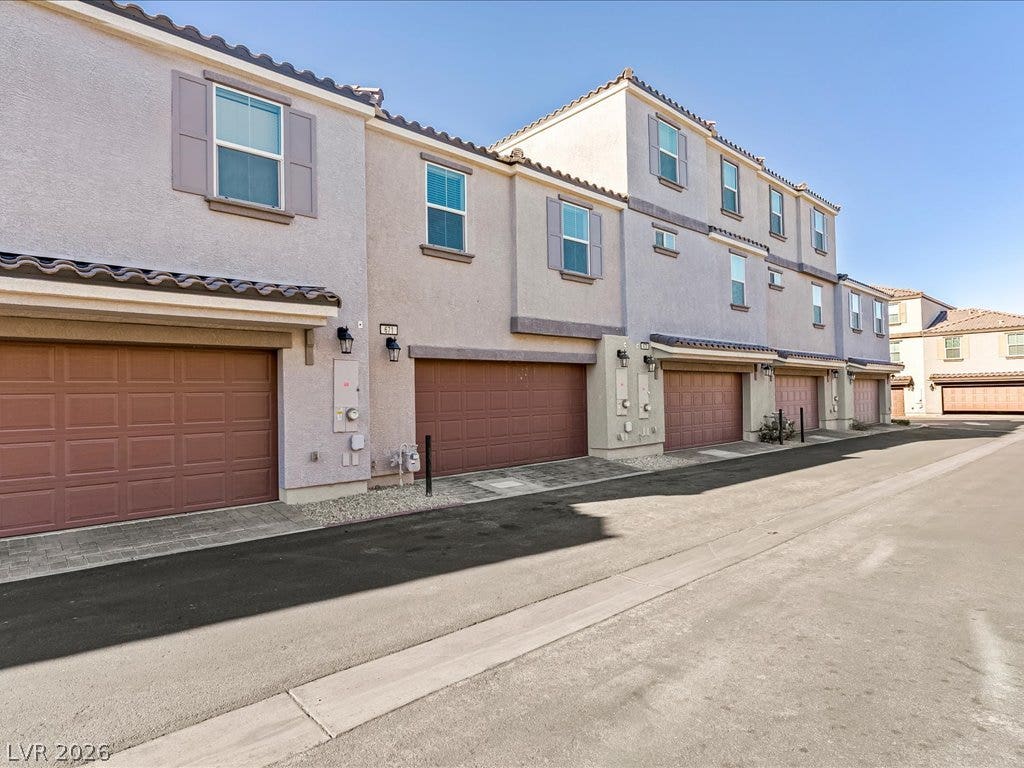 671 Foam Flower Lane, Henderson, NV 89015 Stucco exteriors and tiled rooflines frame the multi-car garage entrances along a paved drive.