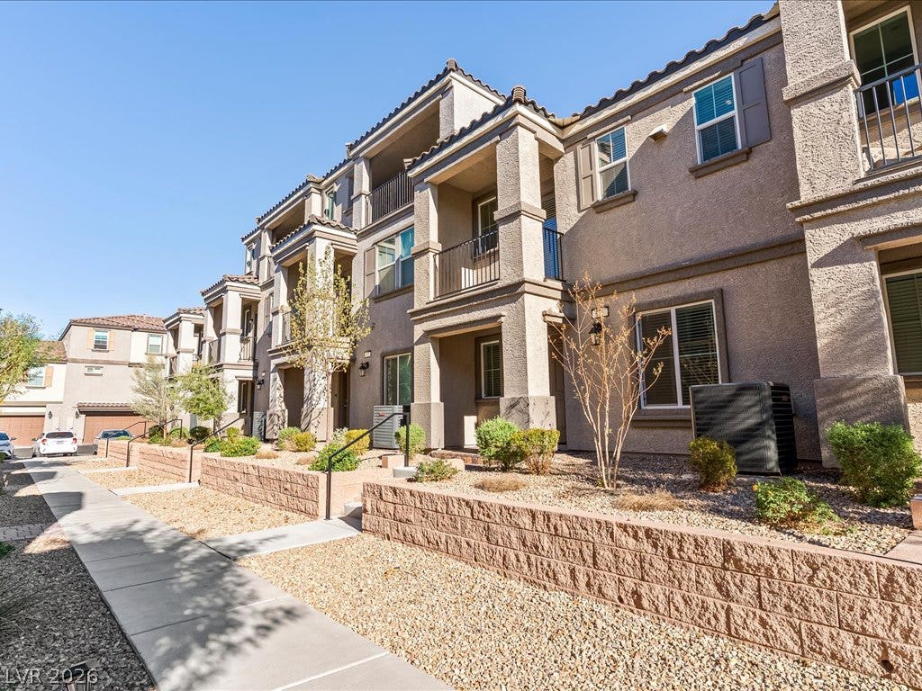 671 Foam Flower Lane, Henderson, NV 89015 Multi-level modern stucco exteriors display private balconies and structured desert landscaping along stone retaining walls.