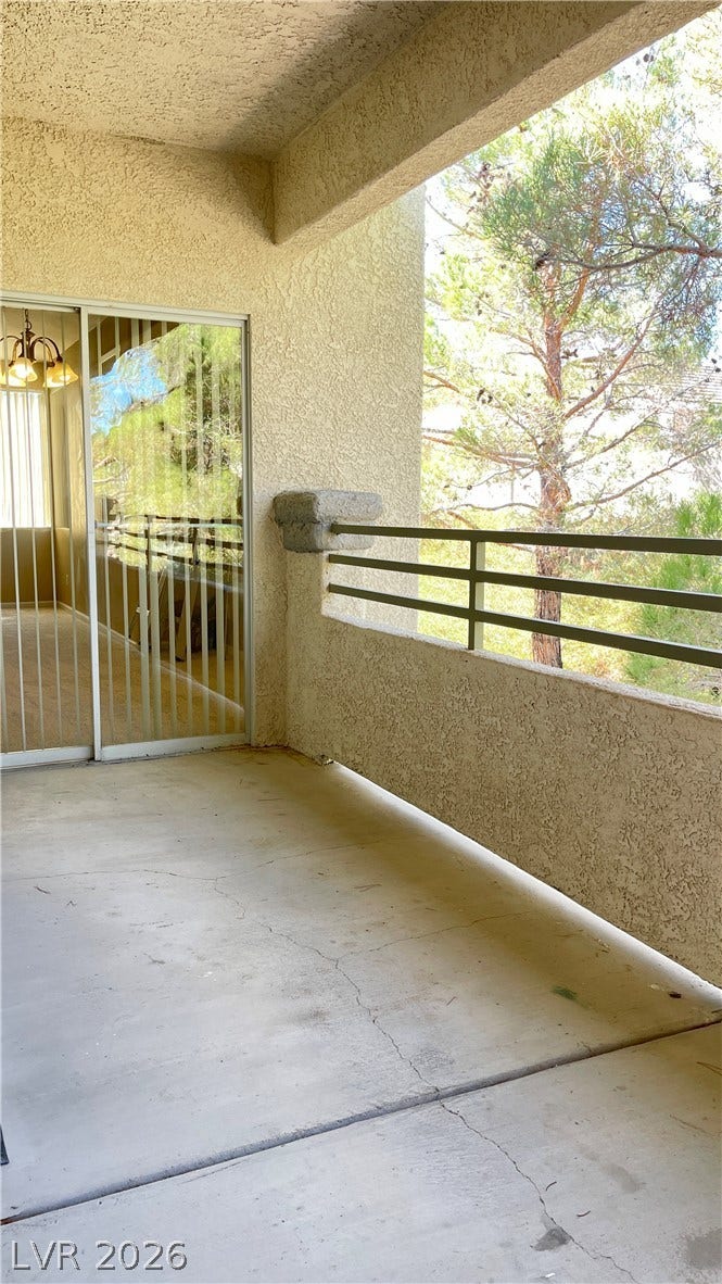 1617 Queen Victoria Street, #201, Las Vegas, NV 89144 A private covered balcony overlooks mature pine trees through sliding glass doors.