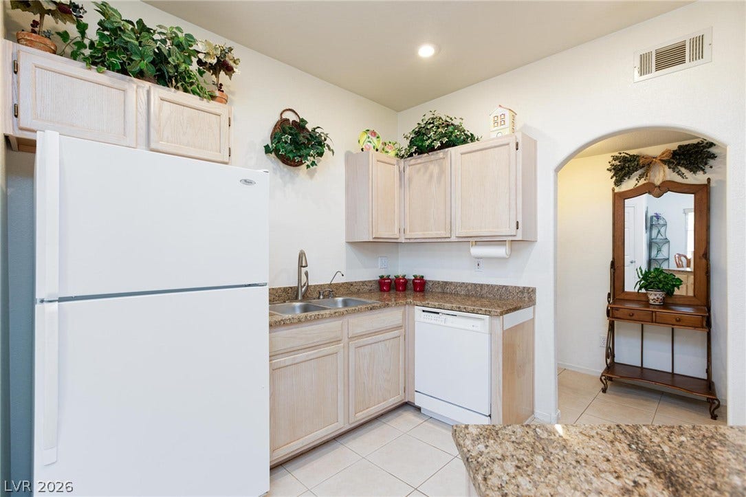 An arched doorway leads to the tiled kitchen featuring granite counters and recessed lighting.