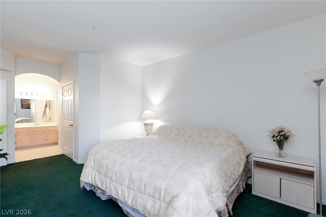 An arched doorway leads from the carpeted bedroom into an adjacent bathroom vanity area.
