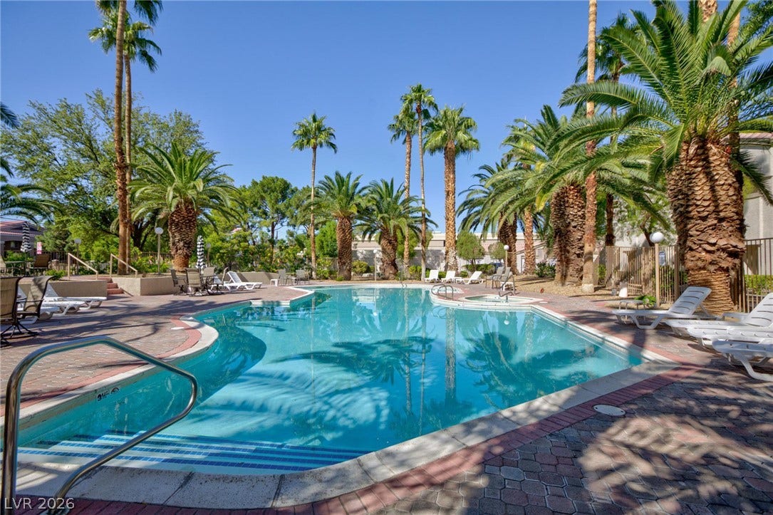 Lush palm trees surround a sparkling blue swimming pool and adjoining hot tub.