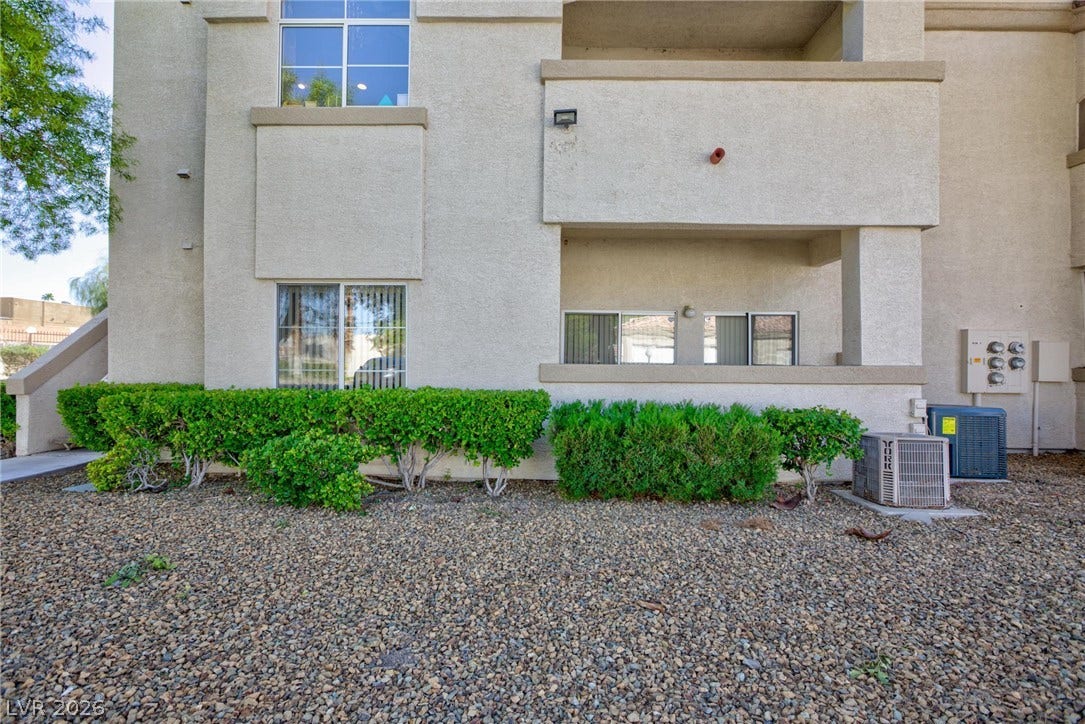 Neat desert landscaping and green hedges border the exterior of this multi-level residential stucco building.