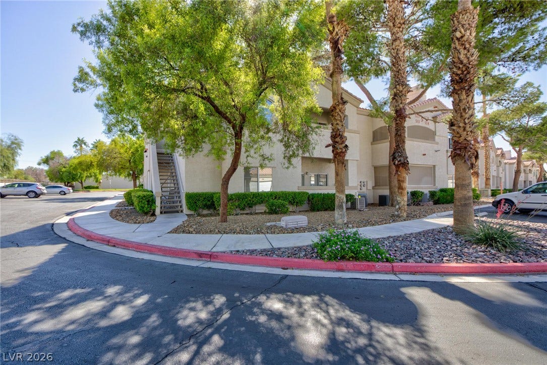 Mature trees shade the concrete pathways leading to this multi-level stucco exterior structure.