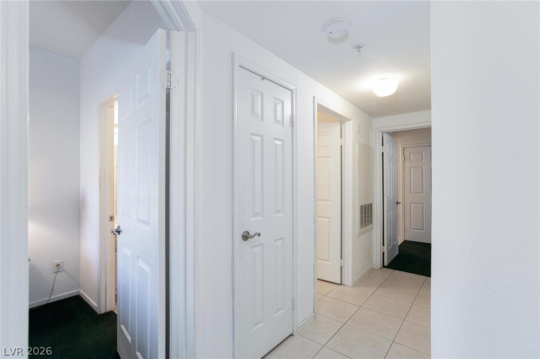 Clean tile flooring transitions to carpet in this centrally located hallway connecting multiple rooms.
