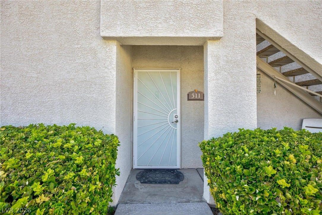 An inviting recessed entryway features a decorative security door flanked by manicured green hedges.